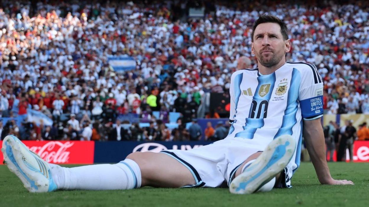 Lionel Messi seated on the pitch in Argentina colours after an international match